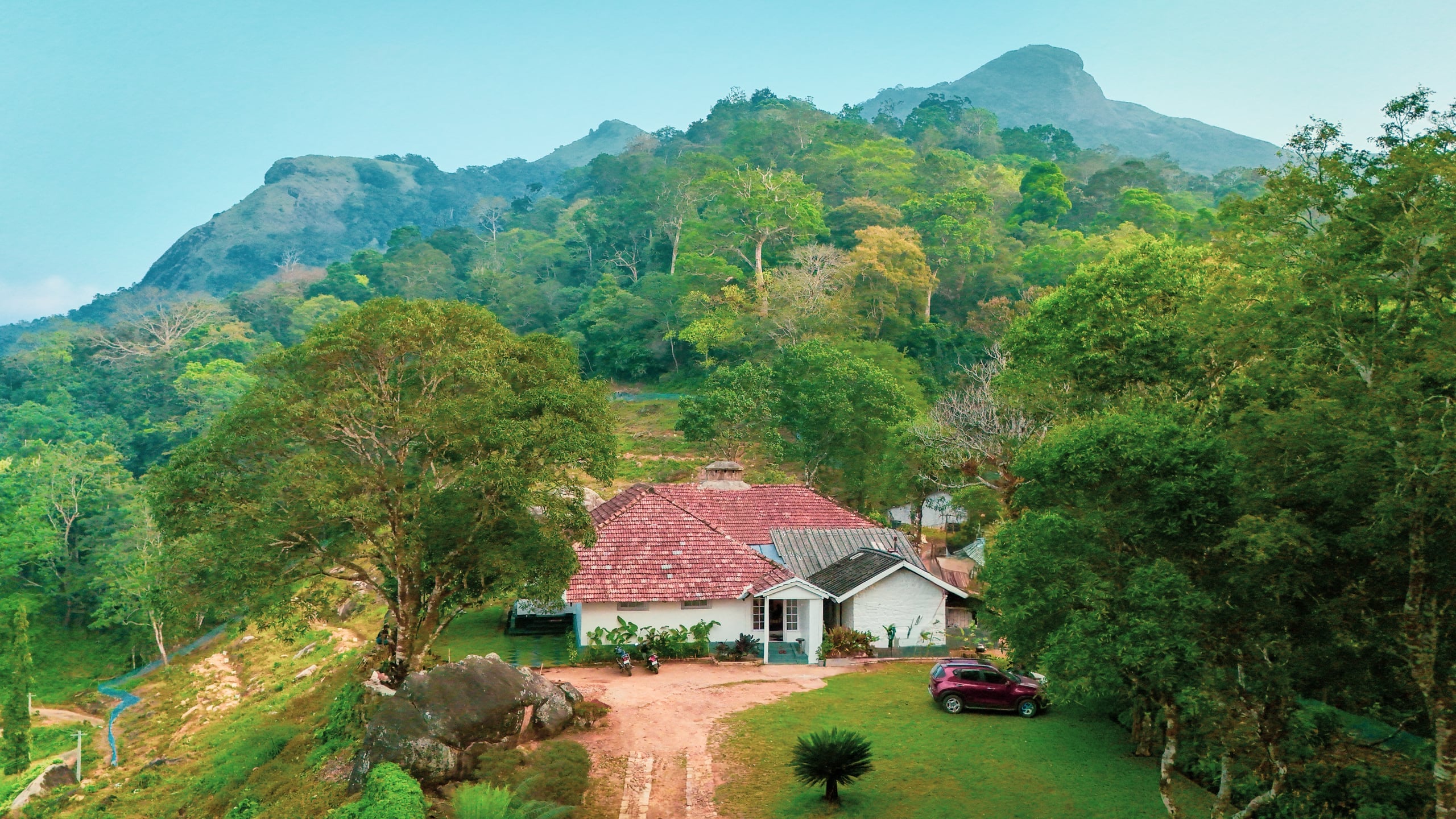 Aerial view of the 1930s bungalow in its plantation estate with hills beyond at Heyday Planter's Portico, near Thenmala, Kollam, Kerala